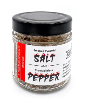 A clear glass jar filled with smoked salt and pepper, sealed with a sleek black lid